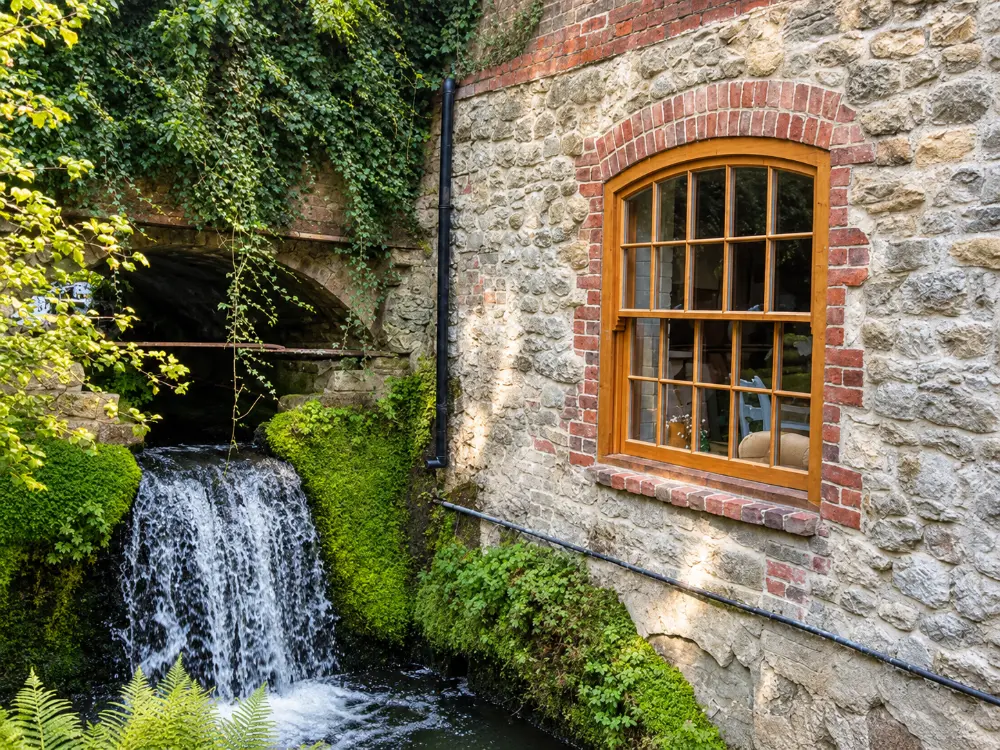 Arched oak window in a stone watermill beside a waterfall, made by Spittlywood
