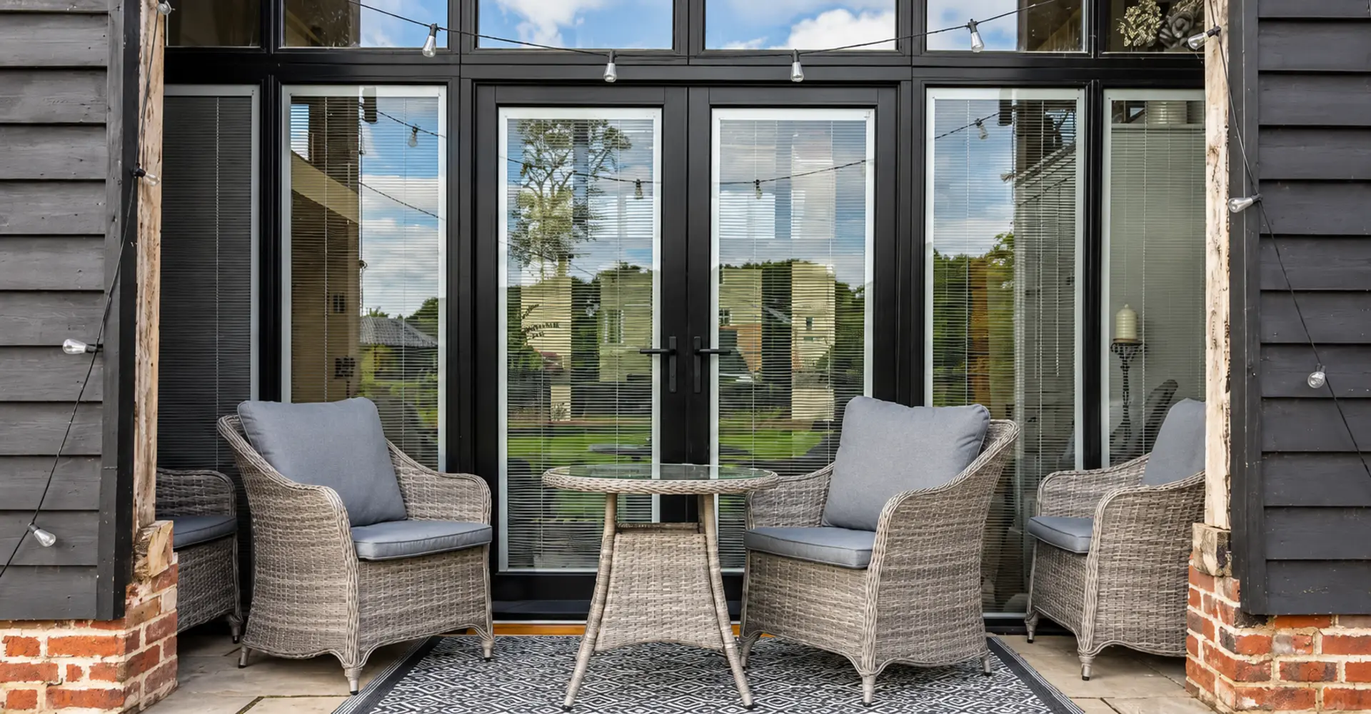 Black timber French doors onto a brick terrace at a barn conversion, made by Spittlywood