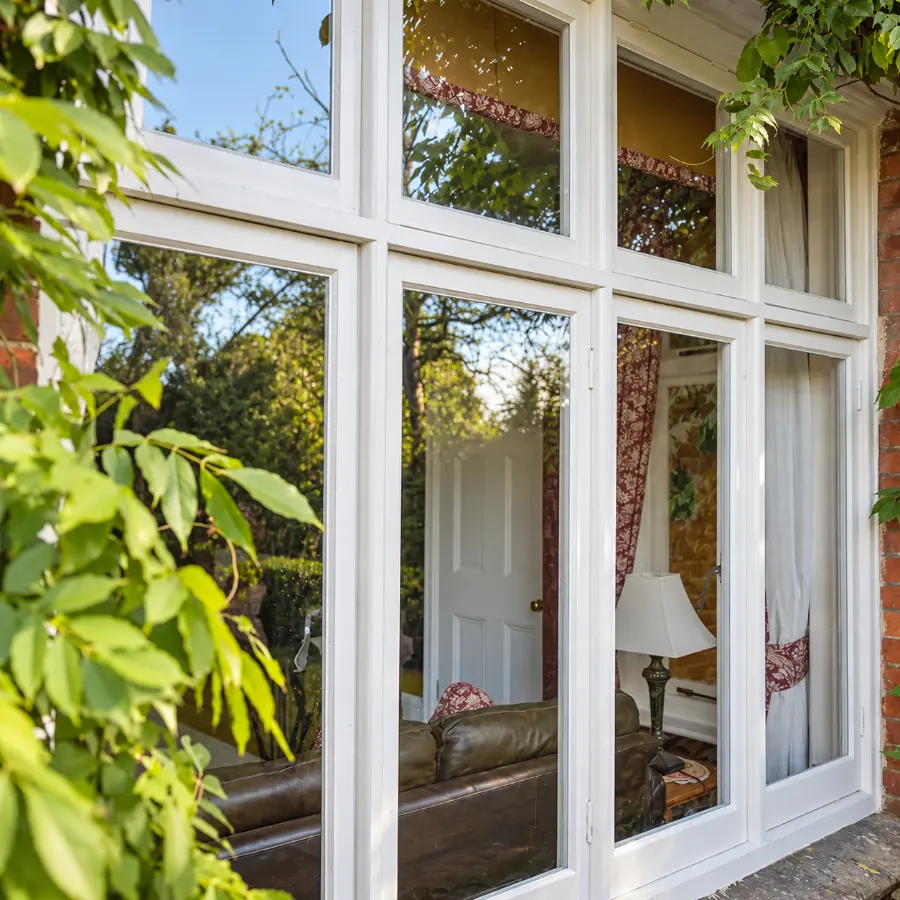 White timber casement windows framed by a climbing plant, made by Spittlywood